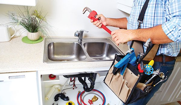 Plumber with pipe wrench and tool bag at a kitchen sink